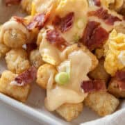 Close up of tater tot totchos with bacon, scallions, eggs, cheese.