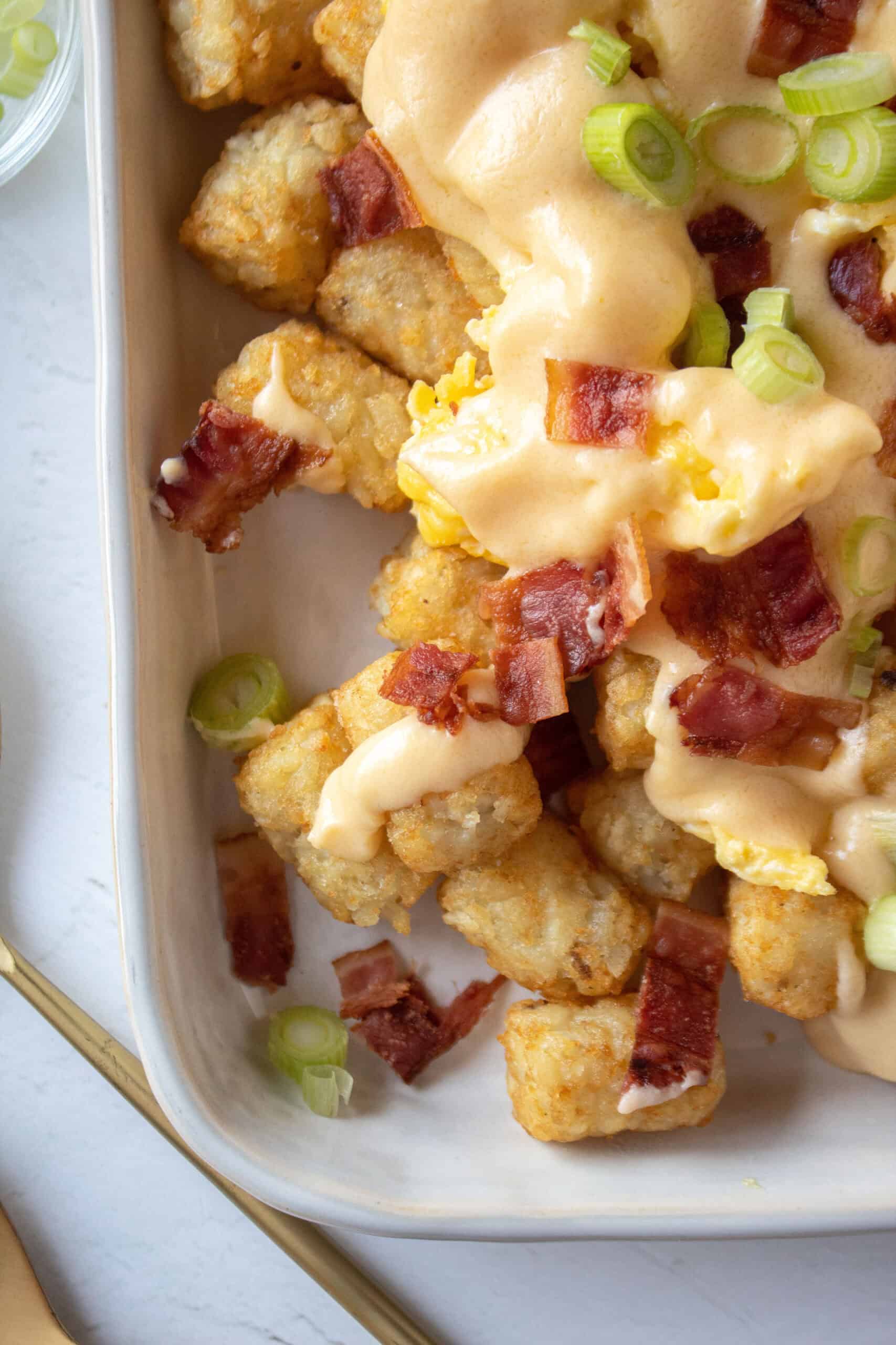 Close up of tater tot totchos with bacon, scallions, eggs, cheese.