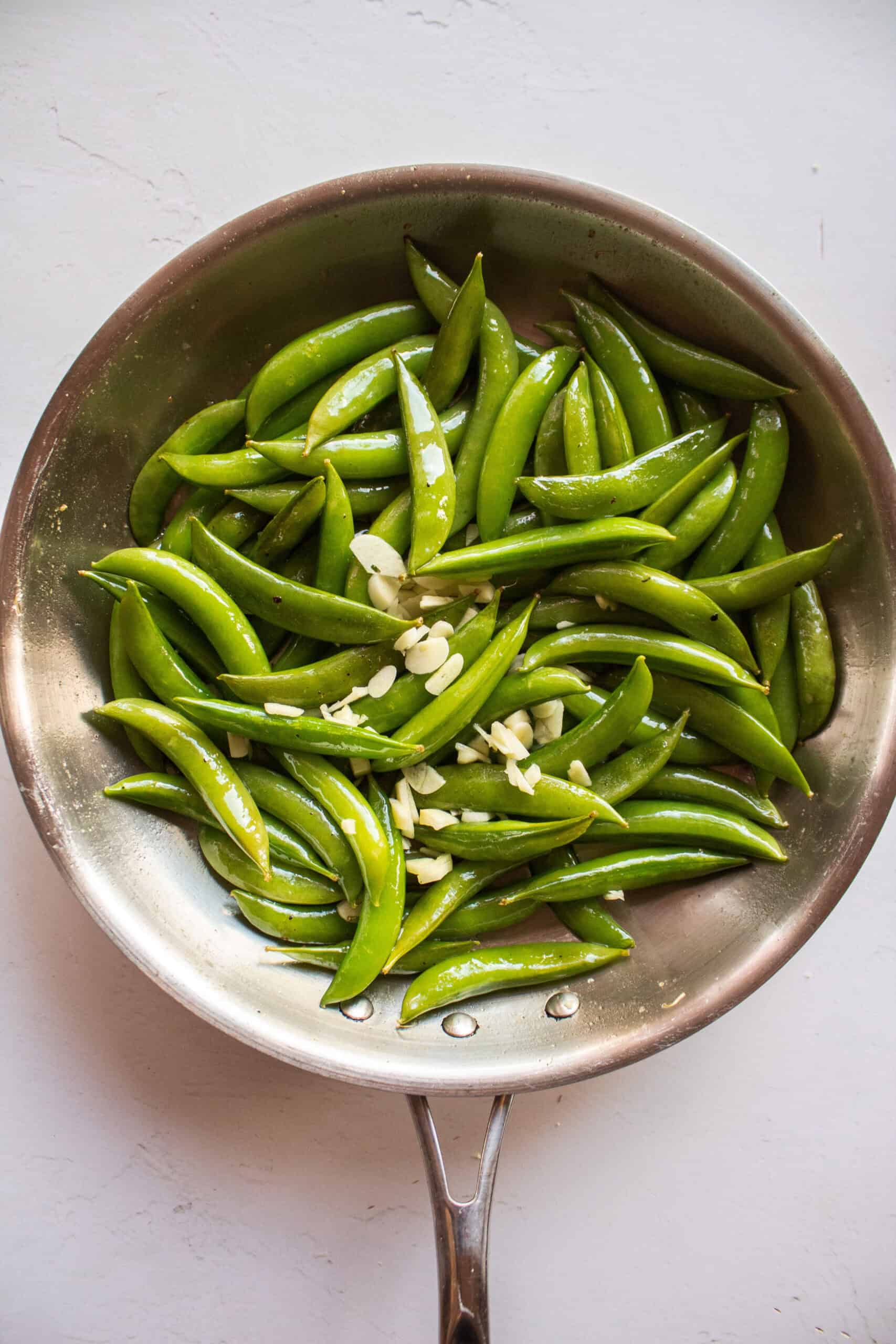 Sugar snap peas in a pan with garlic, oil, salt, and pepper.