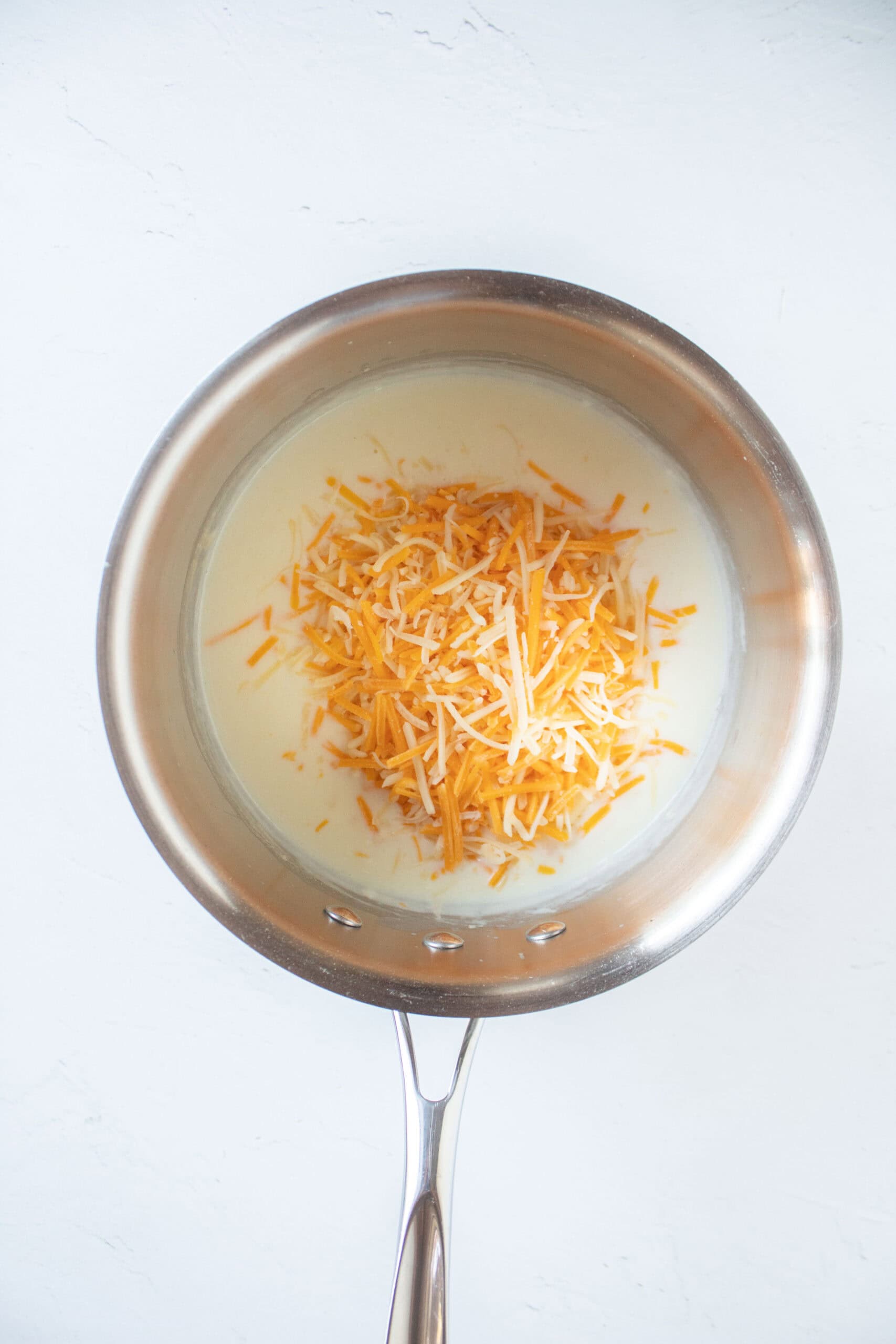 Melted butter in a saucepan with flour, milk, and shredded cheddar cheese to make a cheese sauce.