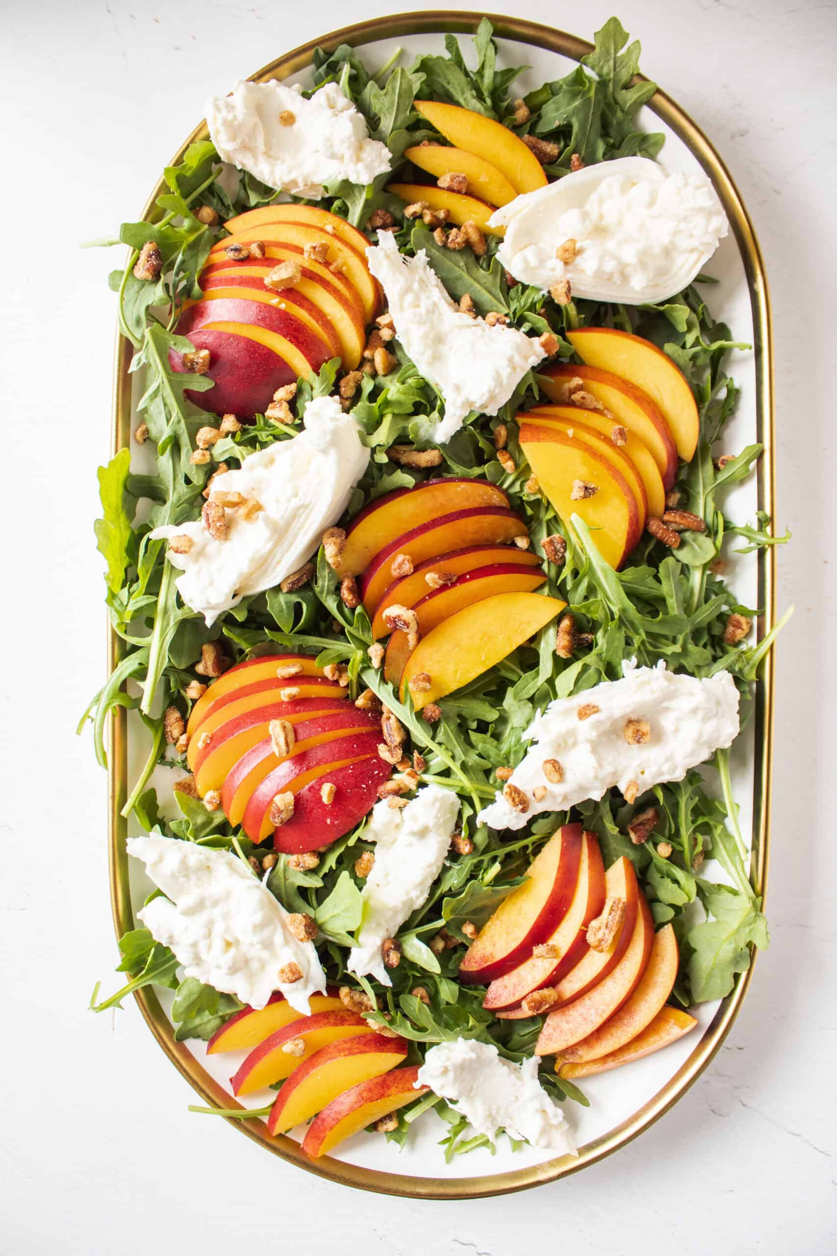 Nectarines and arugula on a platter with burrata topped with pecan pieces.
