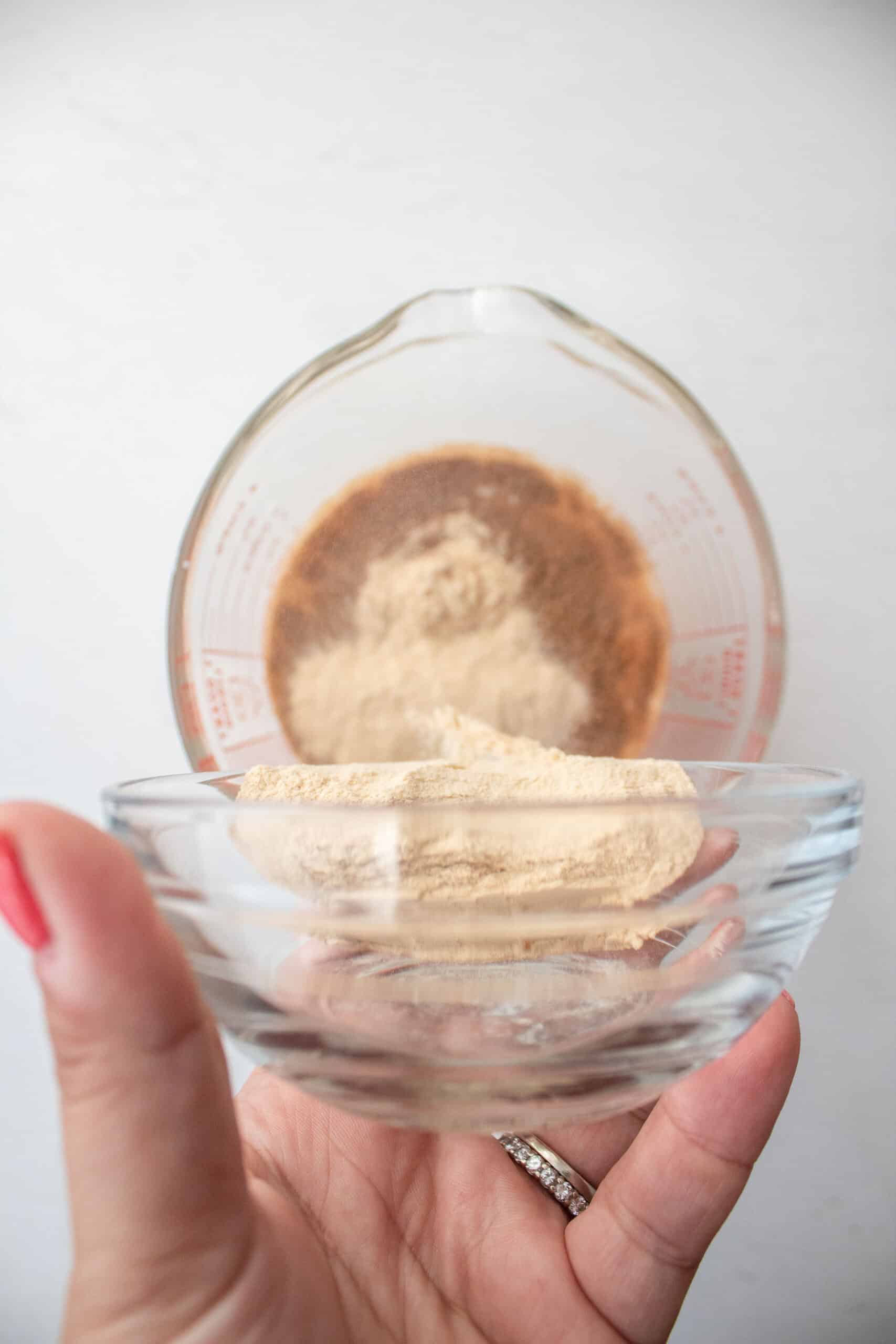 Pumpkin spice bone broth protein powder being poured into a large measuring cup.
