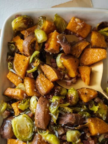 A spoon scooping brussels sprouts and sweet potato on a large platter.