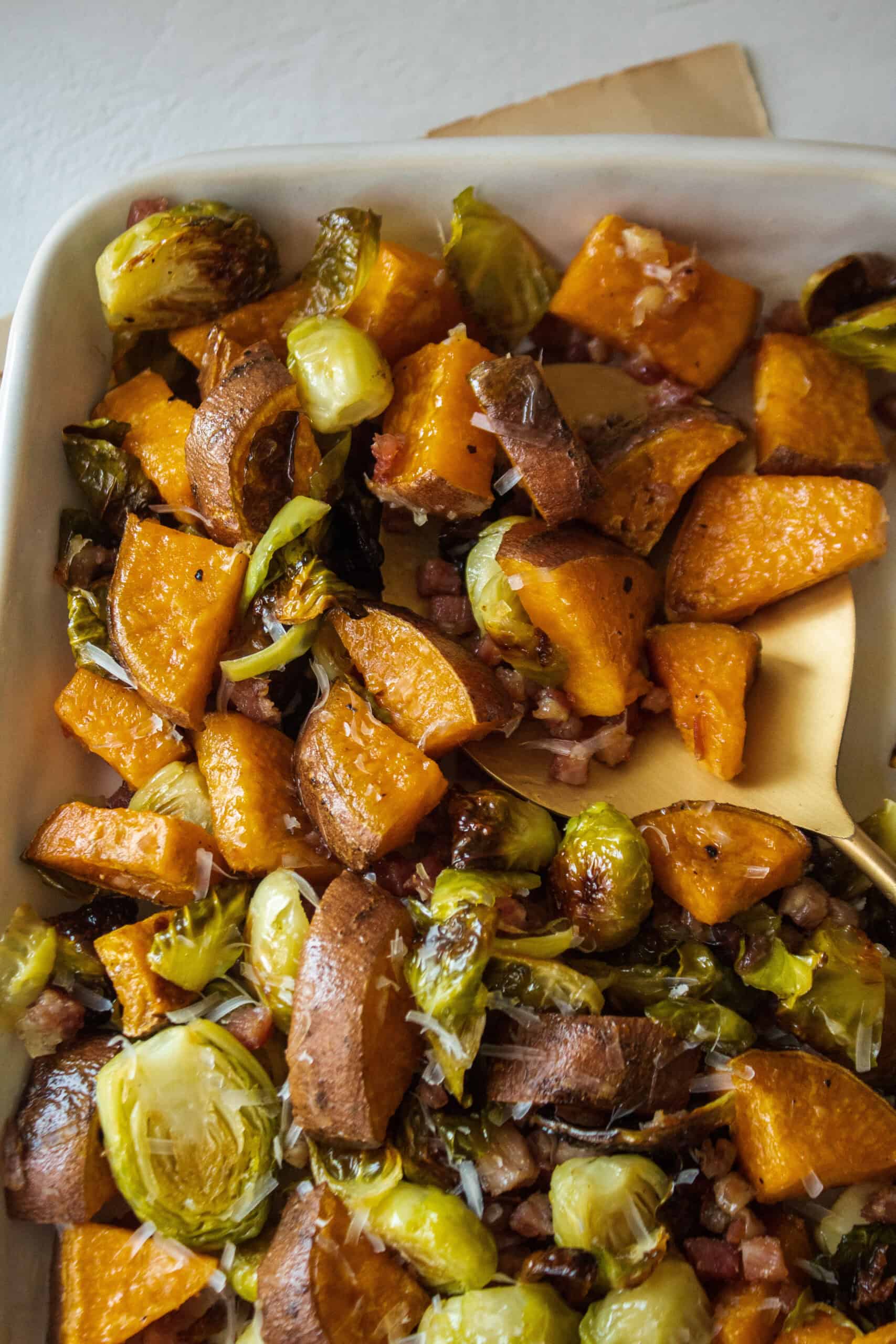 A spoon scooping brussels sprouts and sweet potato on a large platter.