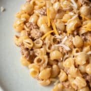 Close up one pot cheeseburger pasta on a plate with cheese and dried pasta around it.