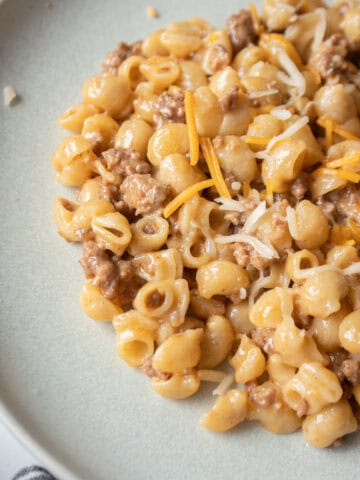 Close up one pot cheeseburger pasta on a plate with cheese and dried pasta around it.