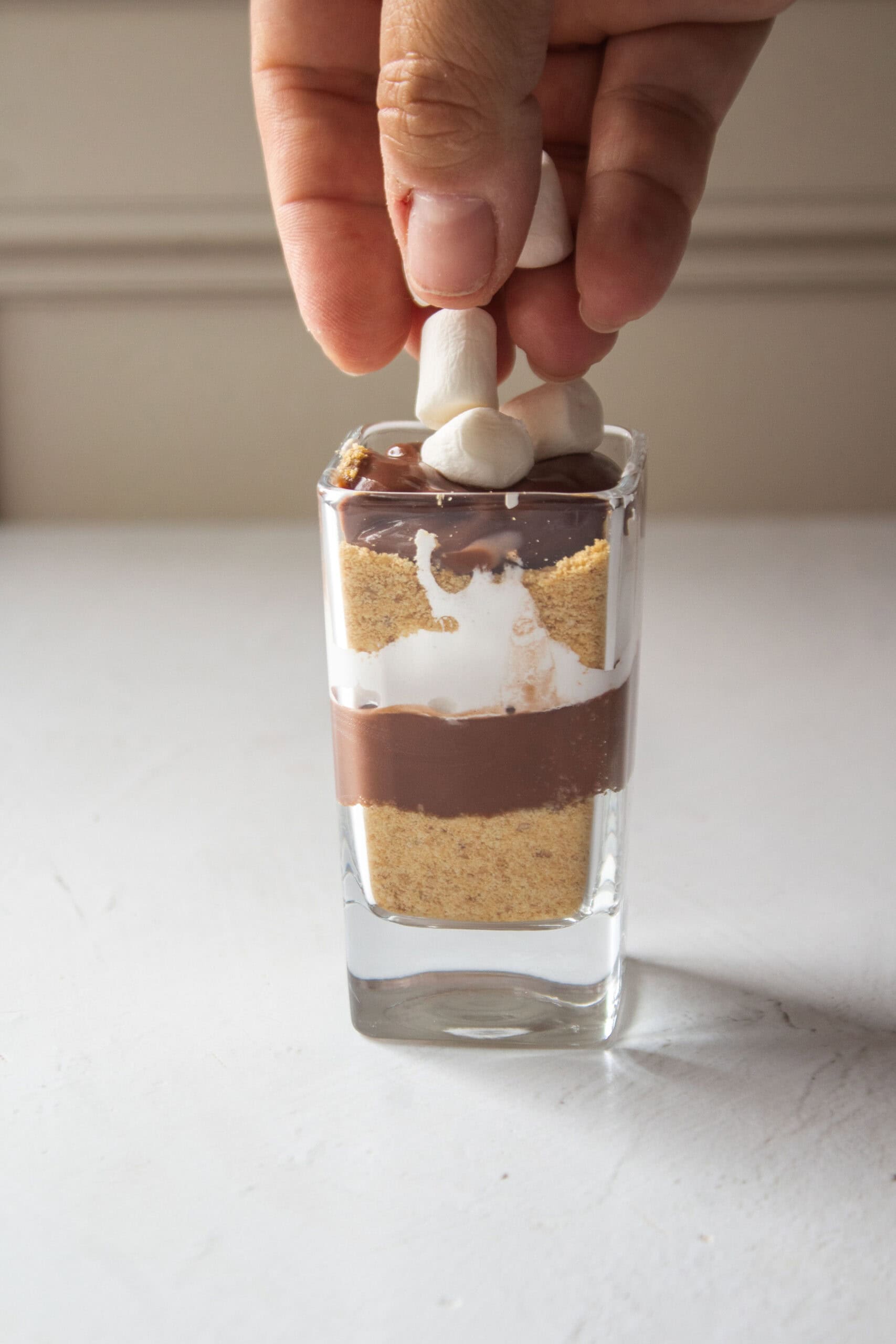Layers of blended graham crackers, pudding, and marshmallow cream inside a shot glass topped with marshmallows.