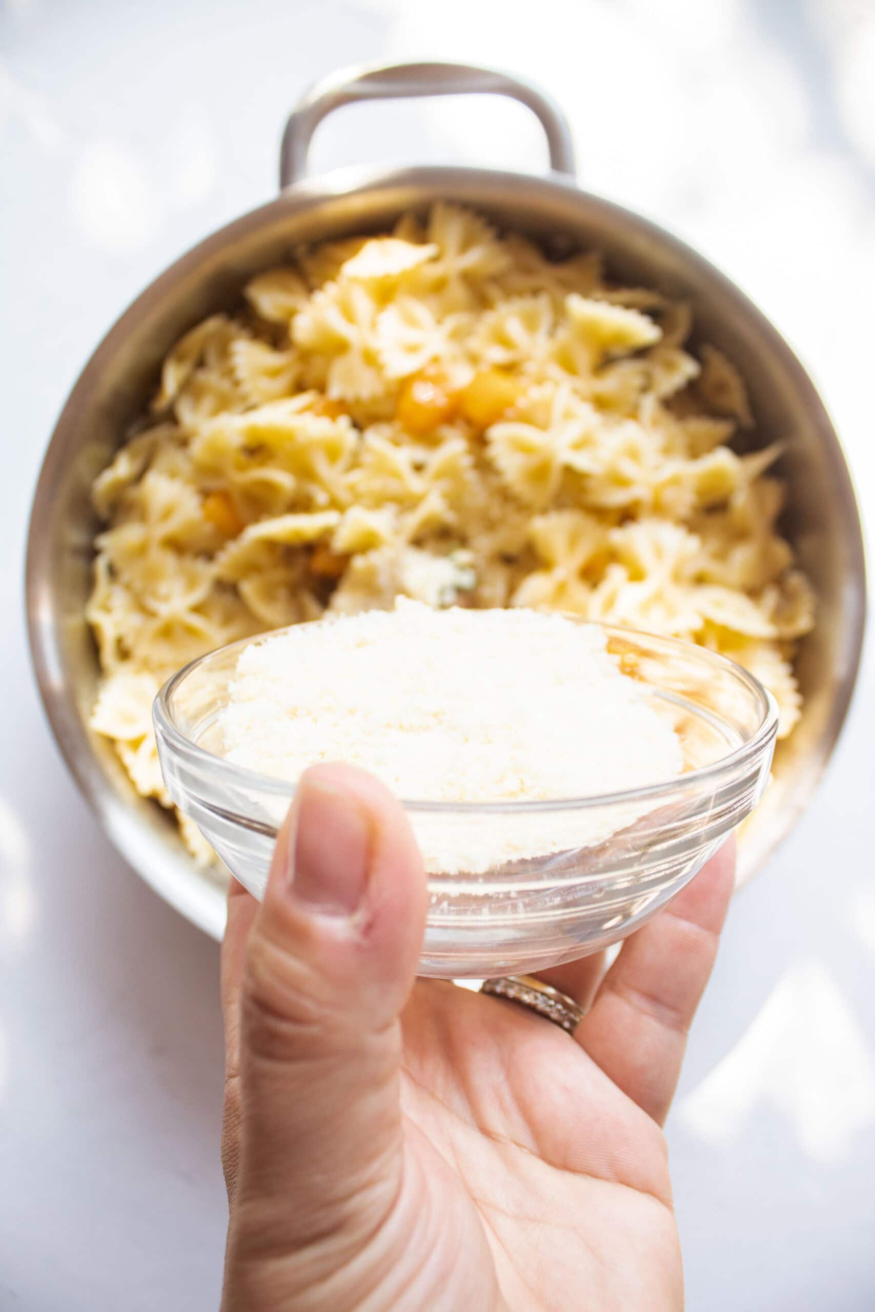 Parmesan cheese sprinkling over the top of farfalle pasta in a pan with butternut squash, butter and sage.