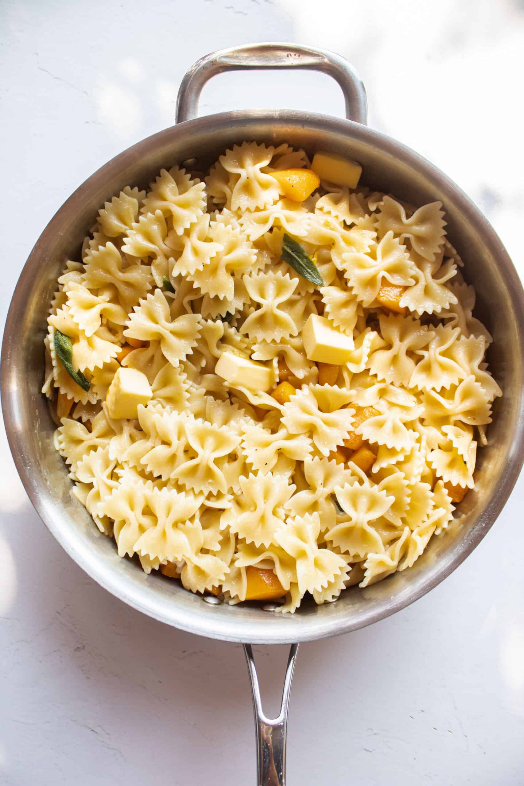 Pasta added to a frying pan with melted butter and butternut squash and sage.