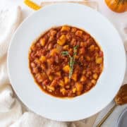 A bowl of fall chili topped with fresh thyme surrounded by loose butternut squash and a pumpkin.