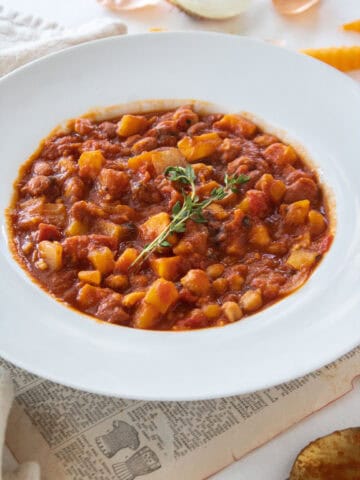 A bowl of fall chili topped with fresh thyme surrounded by loose butternut squash and a pumpkin.