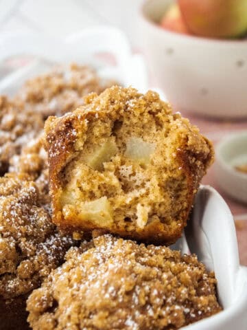 The inside of an apple streusel muffin leaning on its side on top of another muffin in a basket.