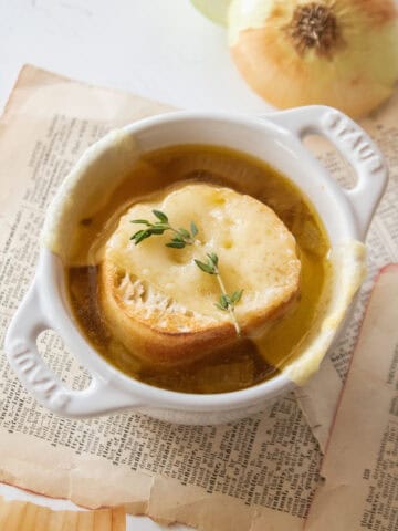 A small dutch oven holding a cup of french onion soup topped with bread, cheese, and thyme.