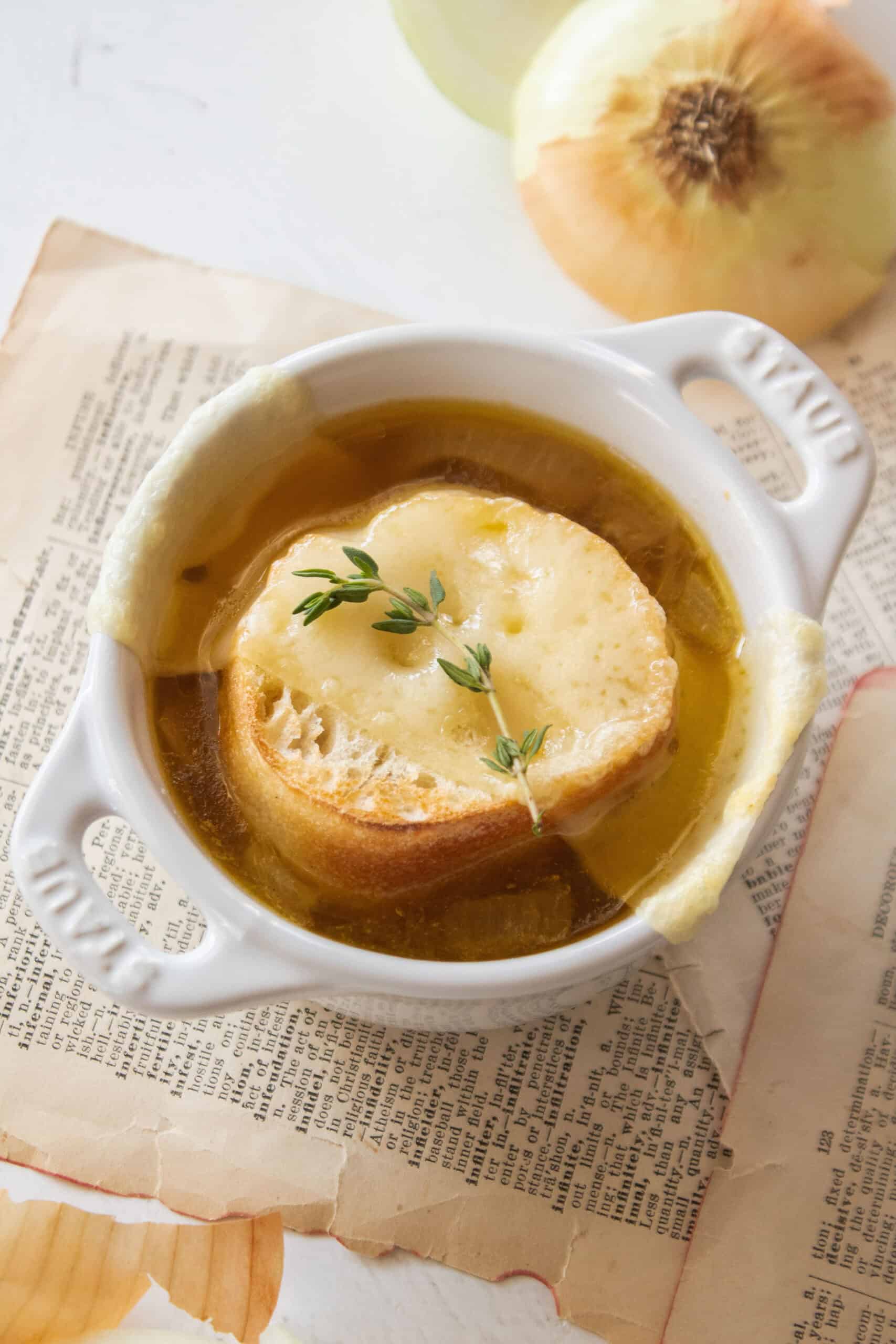 A small dutch oven holding a cup of french onion soup topped with bread, cheese, and thyme.