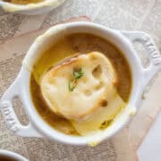 The top of a small dutch oven holding a cup of french onion soup topped with bread, cheese, and thyme.