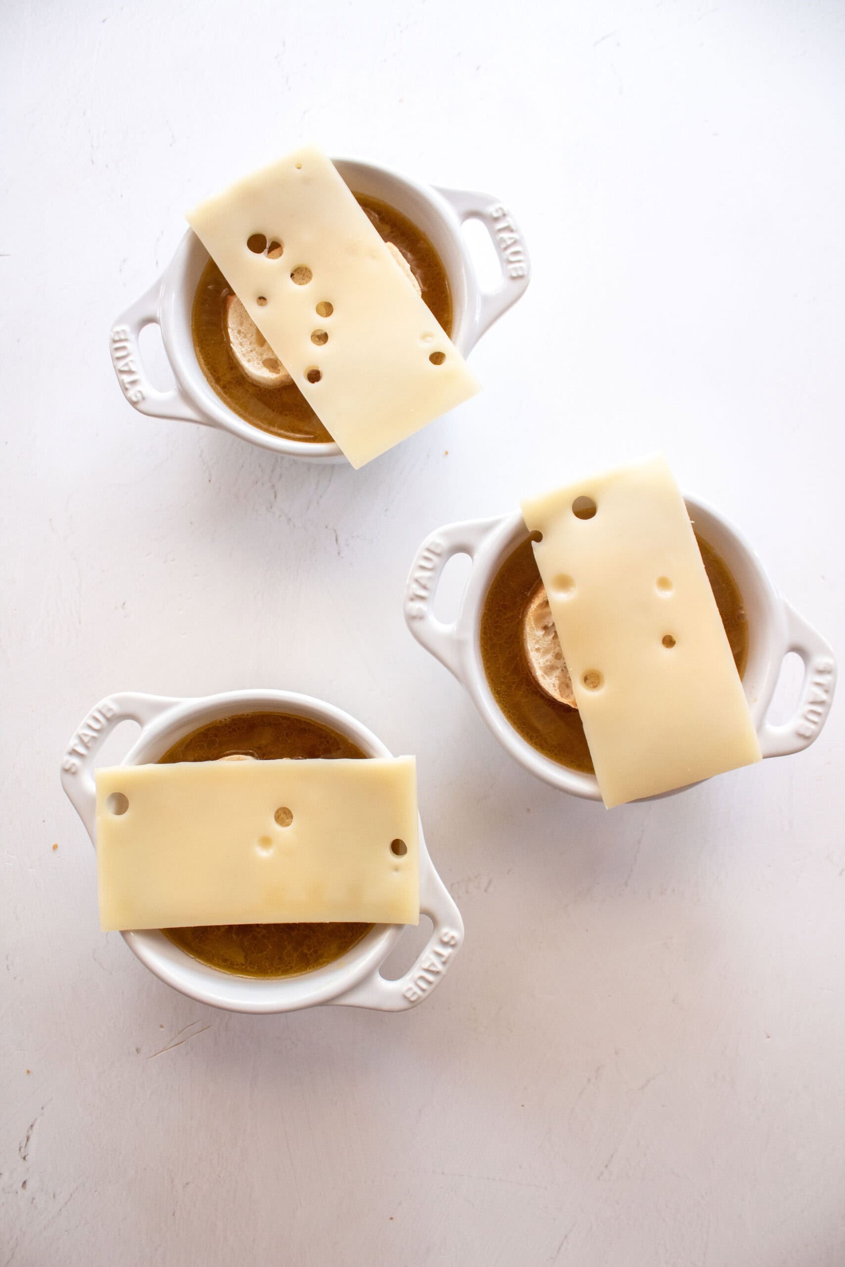 Three small dutch oven cups holding a cup of french onion soup topped with bread and cheese.
