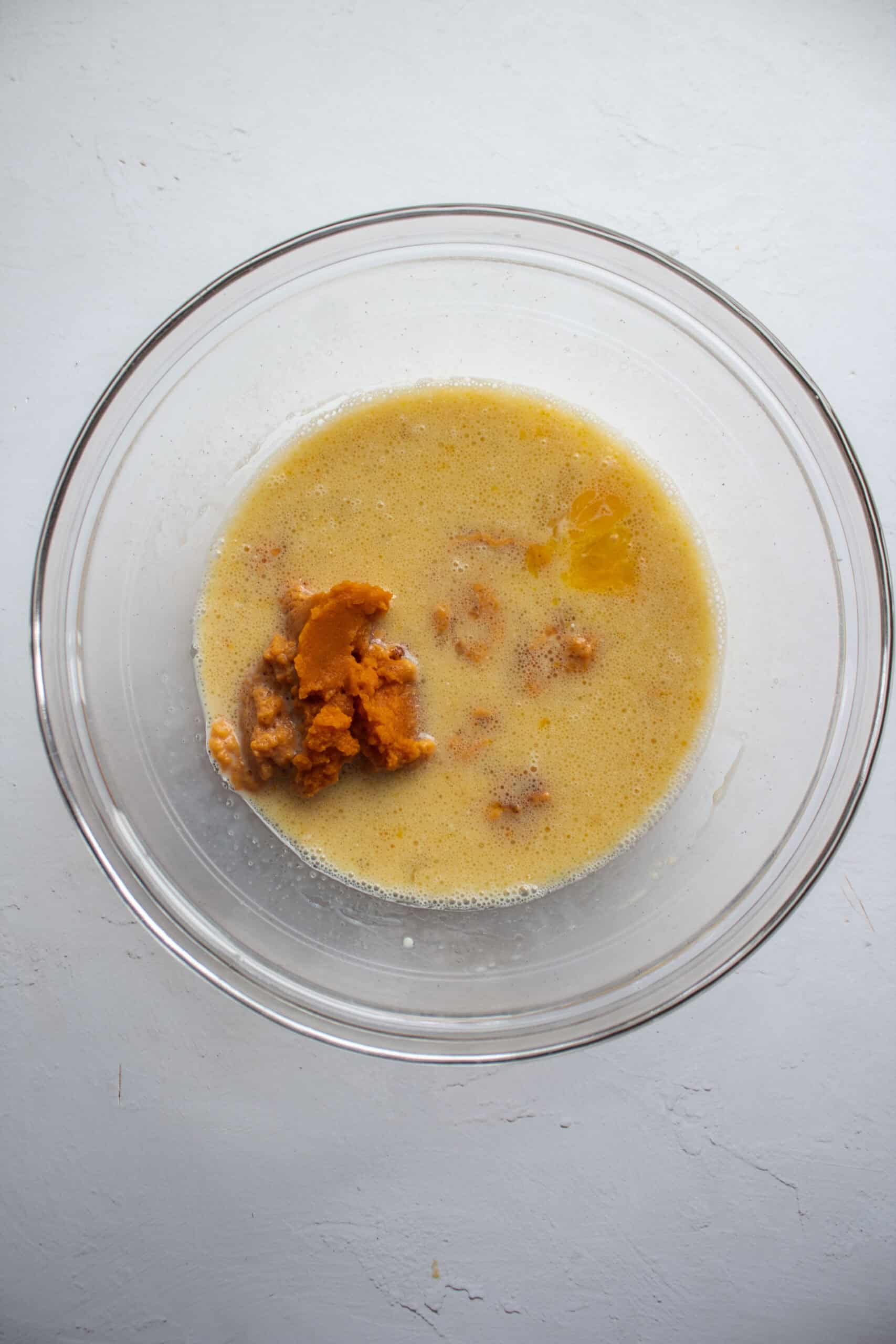 Whisked eggs, oil, milk, vanilla paste, and pumpkin puree in a bowl.
