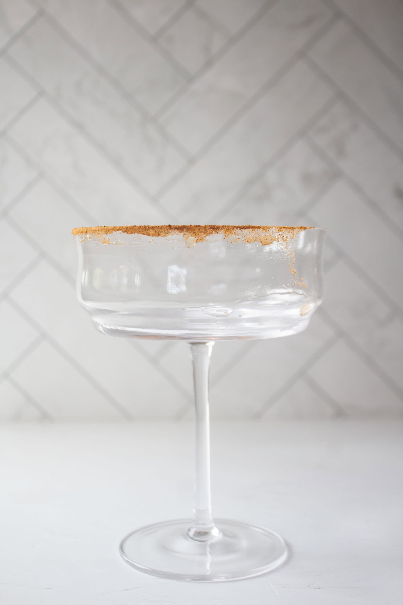 A martini coupe glass with a dusting of pumpkin pie spice on the rim of the glass.