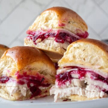 A stack of three turkey cranberry sliders on top of each other on a plate.
