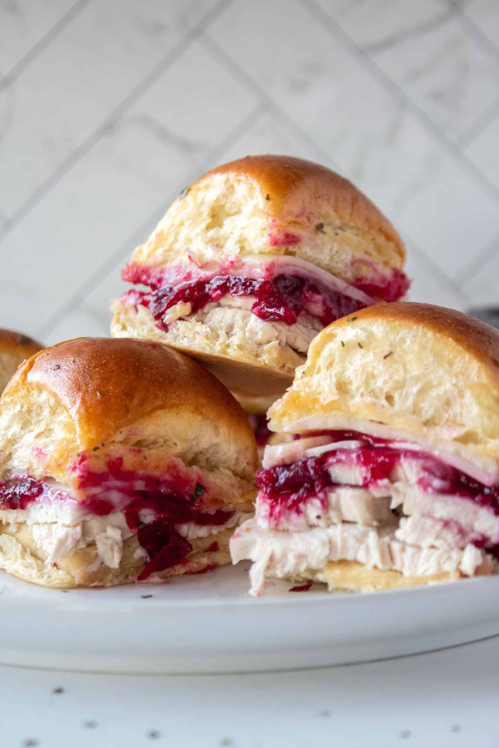 A stack of three turkey cranberry sliders on top of each other on a plate.