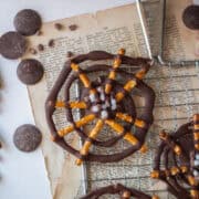 Close up of a chocolate pretzel spider web on a cooling rack with cacao wafers around it.