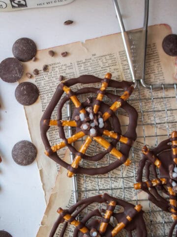 Close up of a chocolate pretzel spider web on a cooling rack with cacao wafers around it.