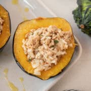 Close up of an acorn squash stuffed with ground turkey and rice and a gourd in the background.