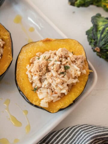 Close up of an acorn squash stuffed with ground turkey and rice and a gourd in the background.