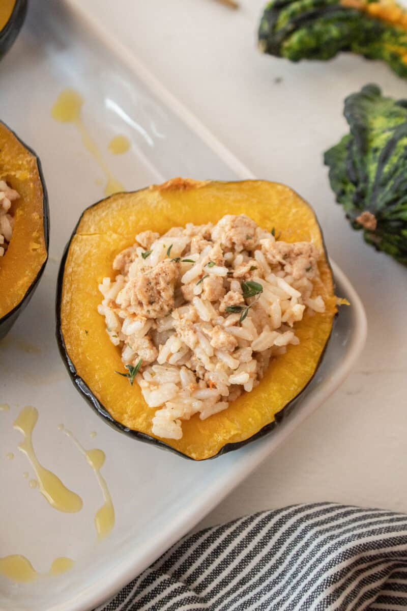 Close up of an acorn squash stuffed with ground turkey and rice and a gourd in the background.