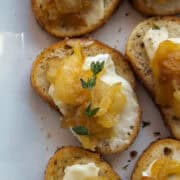 Close up on on a caramelized onion brie crostini topped with thyme on a platter.