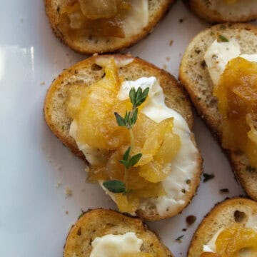 Close up on on a caramelized onion brie crostini topped with thyme on a platter.