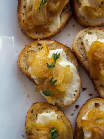 Close up on on a caramelized onion brie crostini topped with thyme on a platter.