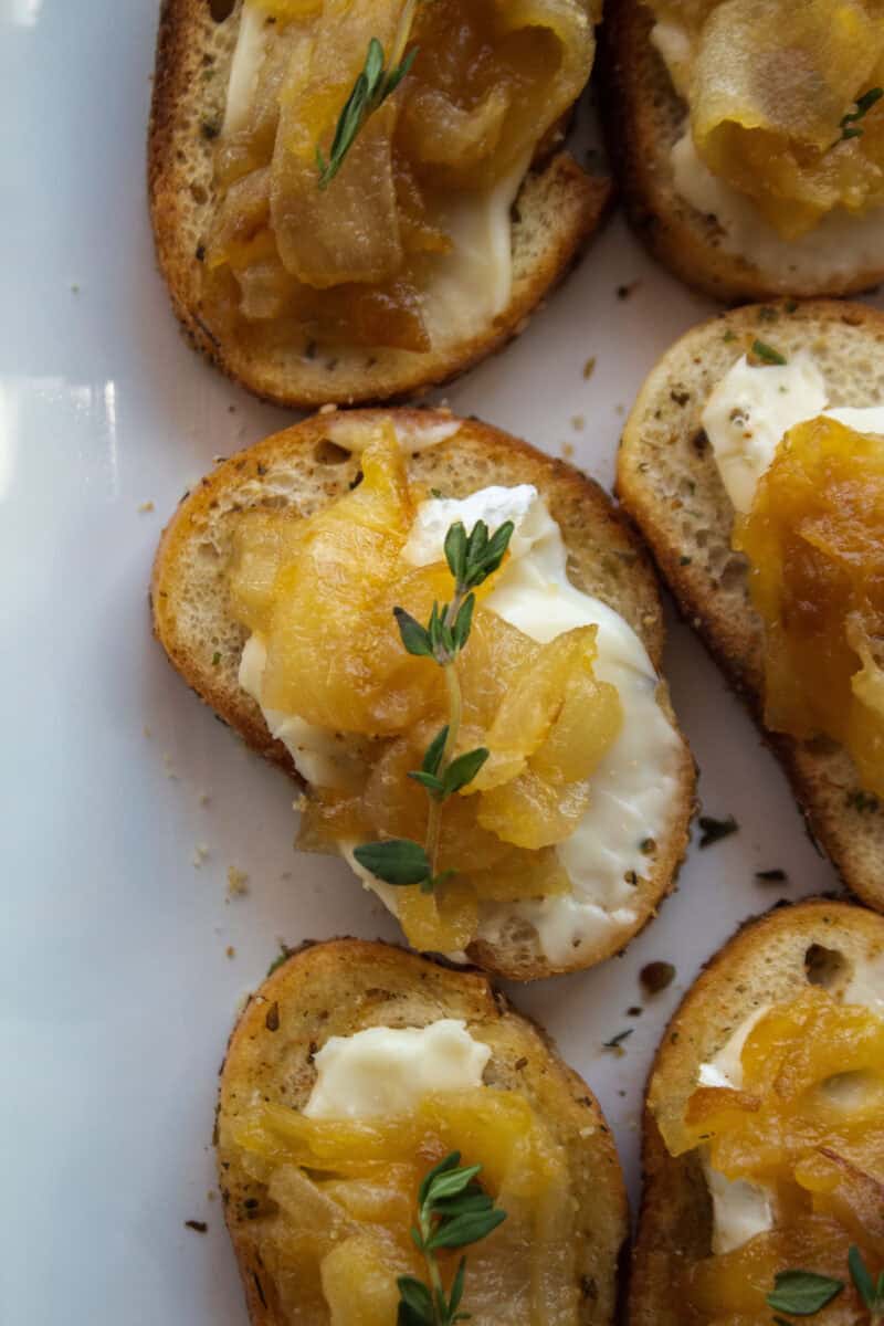 Close up on on a caramelized onion brie crostini topped with thyme on a platter.