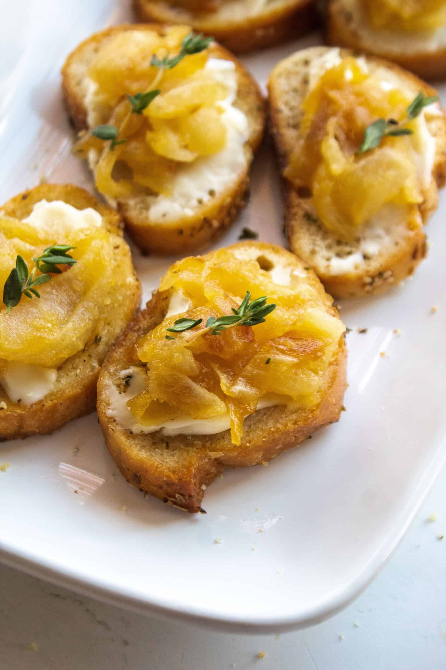 Close up on on a caramelized onion brie crostini topped with thyme on a platter.