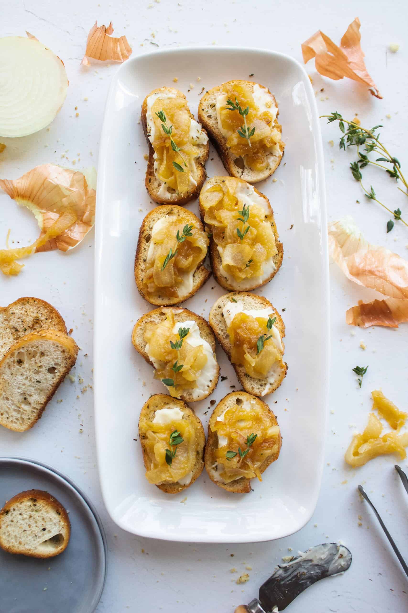 Eight caramelized onion brie crostini on a platter with thyme.