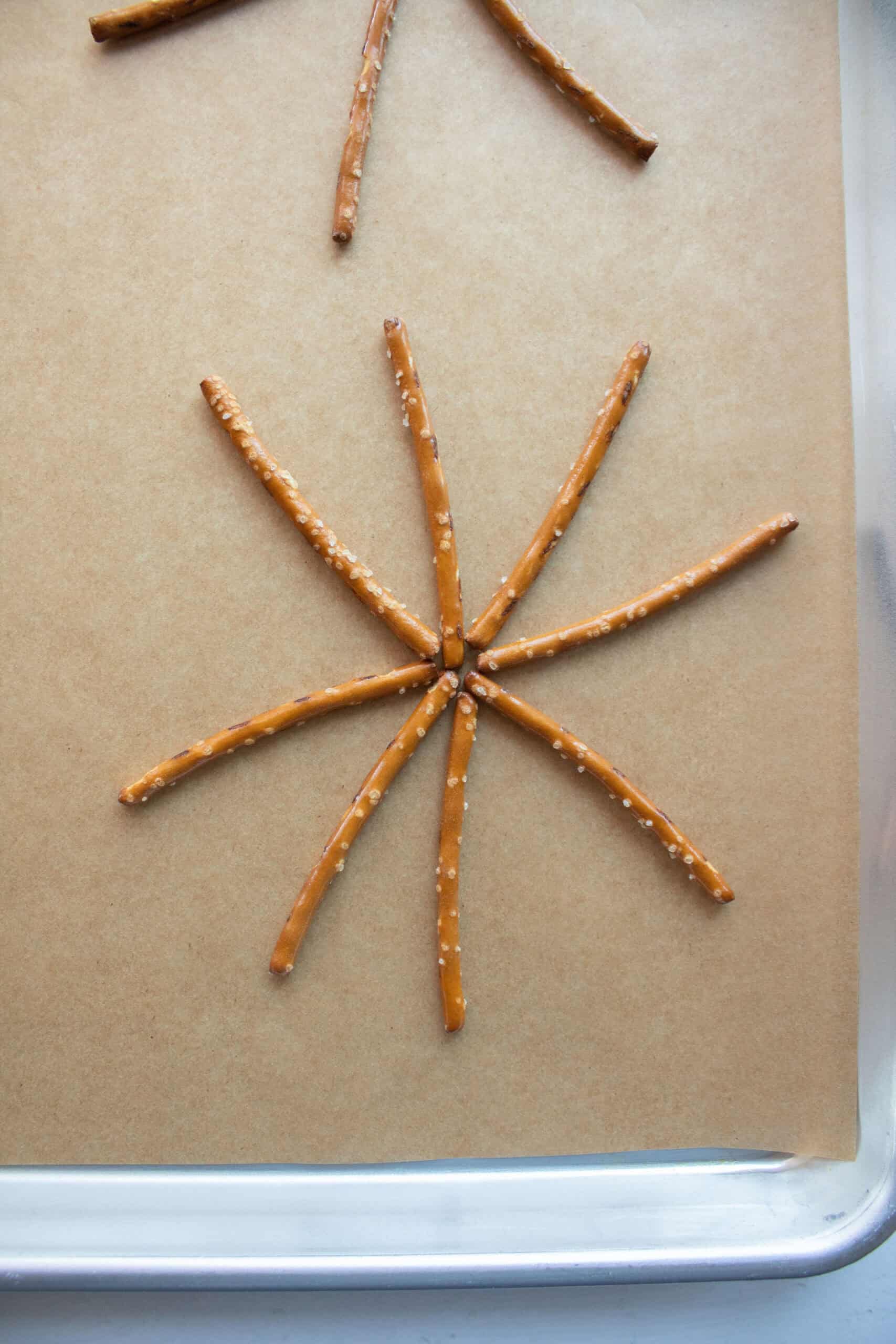 Eight mini pretzel sticks shaped in a spider web on parchment paper.