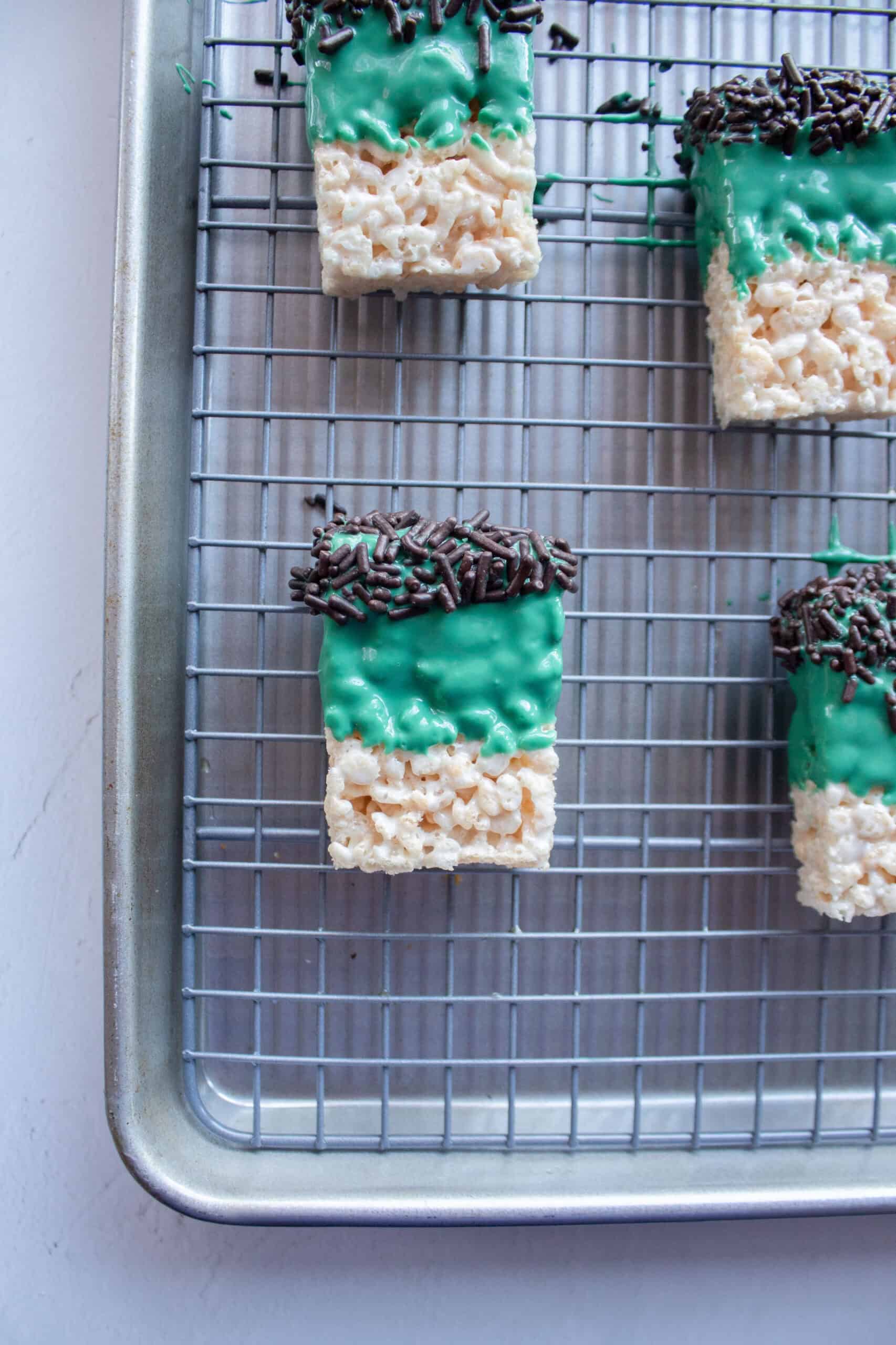 Four rice krispie treats dipped into green melting chocolate with sprinkles at the top.