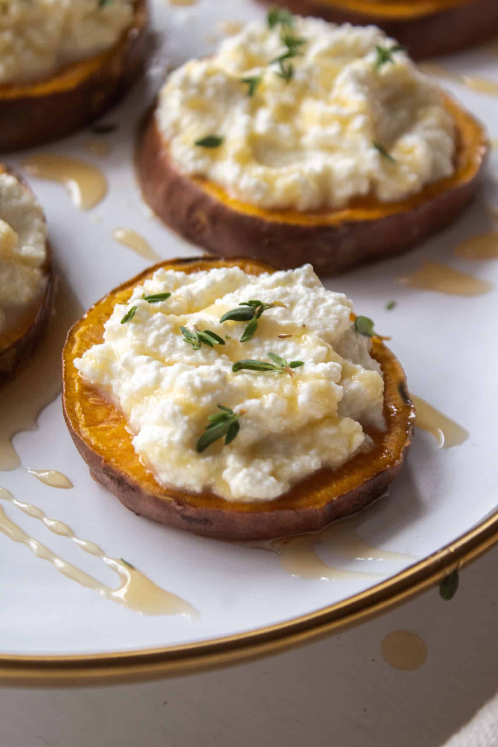 High angle shot of a sweet potato round topped with ricotta, thyme, and honey on a plate surrounded by other sweet potato rounds.