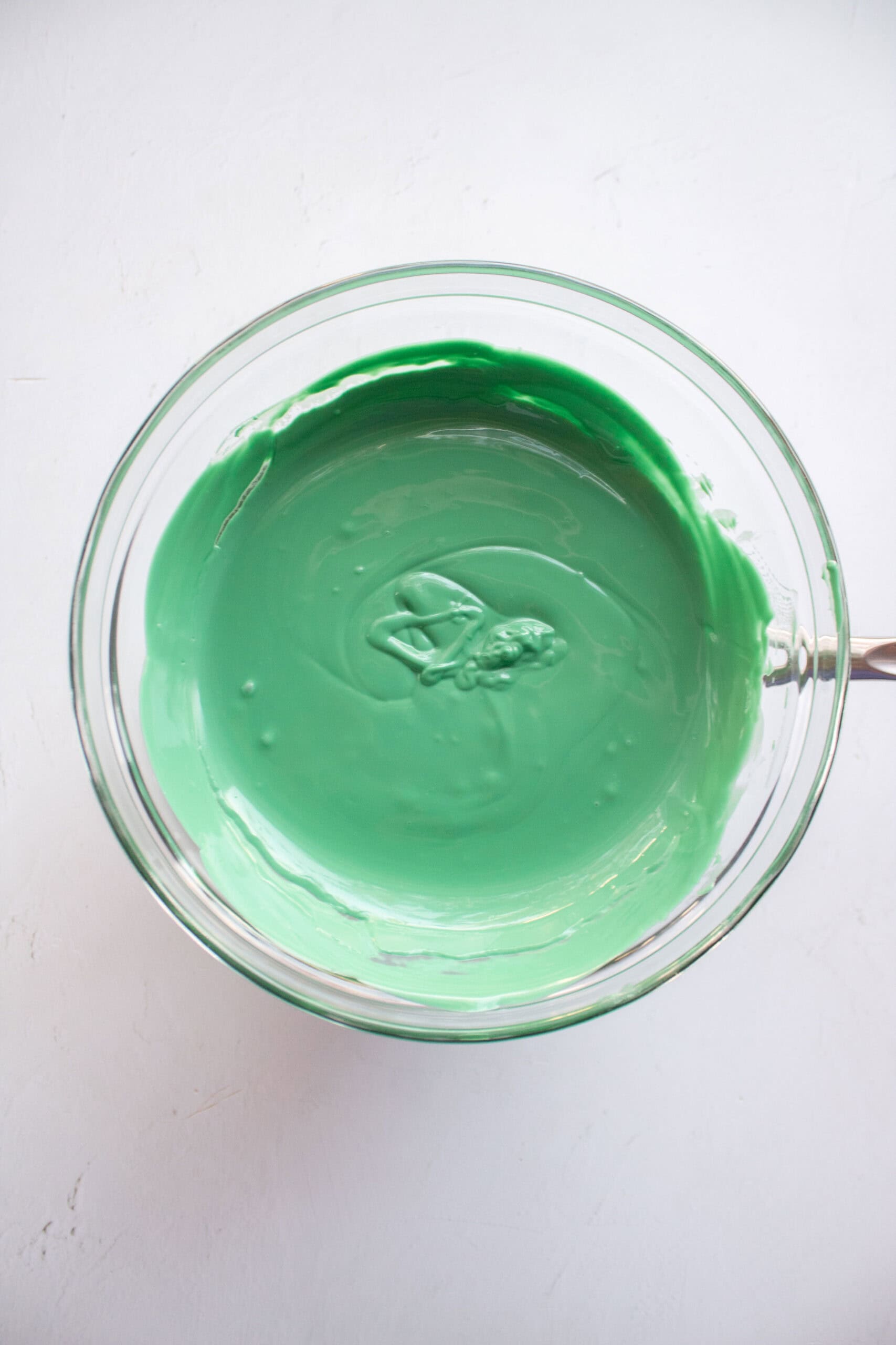 Green melted chocolate in a large glass bowl over a small pot of boiling water.