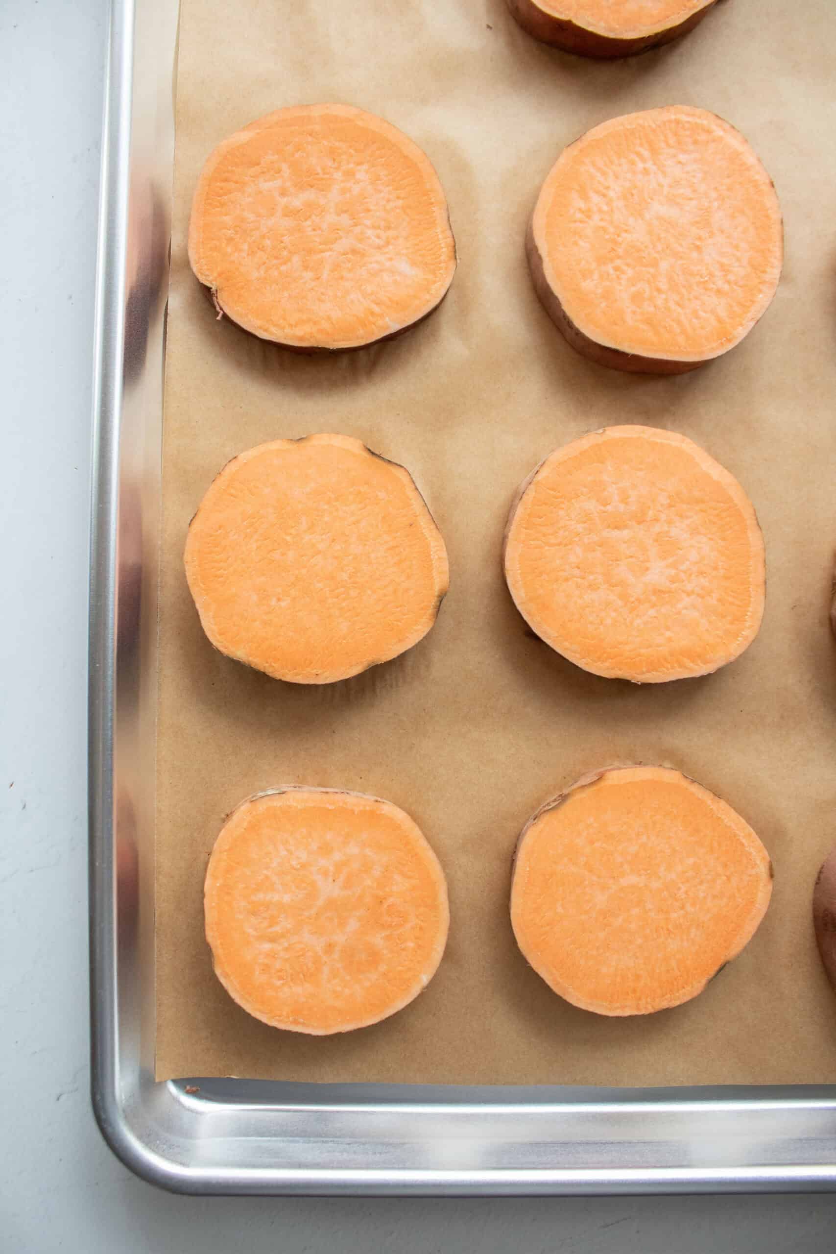 Seven sweet potato slices on a baking sheet before going into the oven without oil.