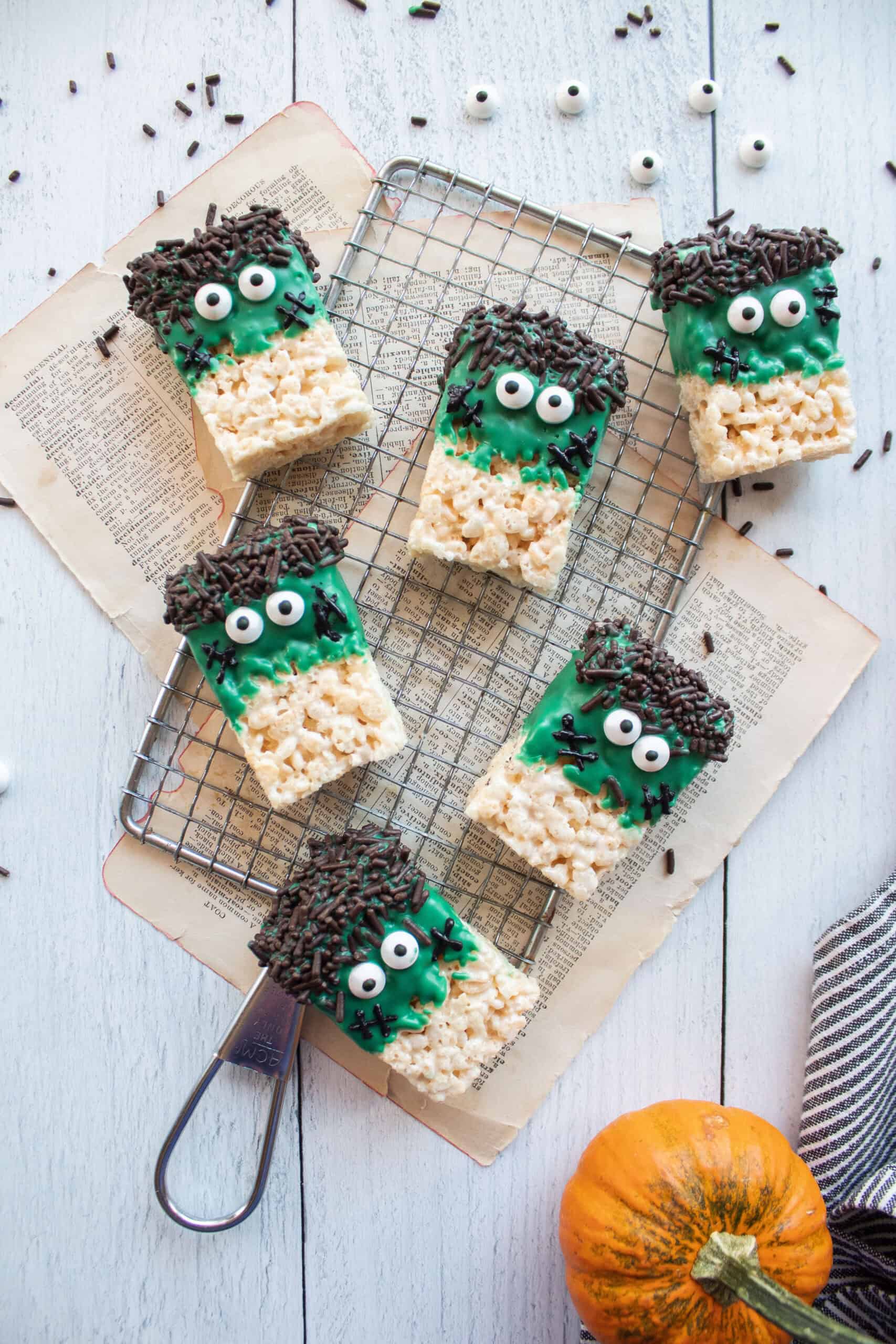Six rice krispie treats dipped into green melting chocolate with sprinkles and stitches on a cooling rack.