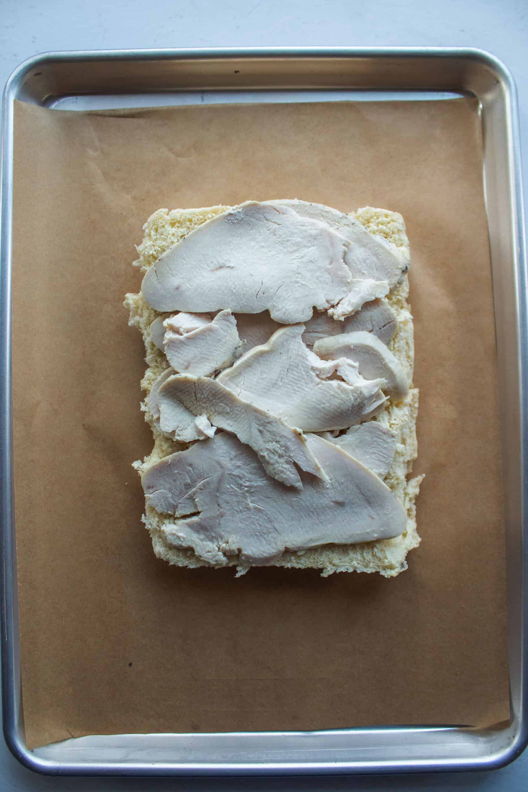 Sliced oven roasted turkey on the bottom half of hawaiian rolls on a baking sheet.