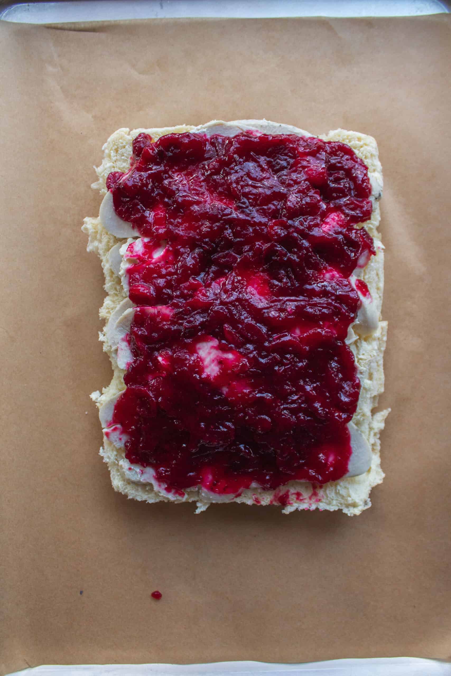 Sliced turkey and cranberry sauce on the bottom half of hawaiian rolls on a baking sheet.