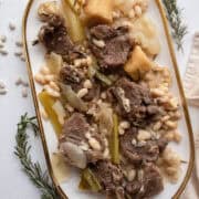 Braised lamb loin chops with white beans on a platter with braised vegetables and rosemary.