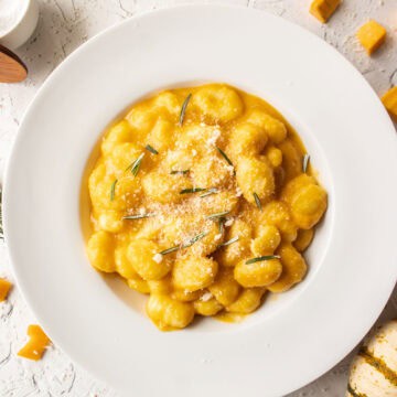 Butternut squash pasta gnocchi in a bowl topped with parmesan cheese and rosemary.