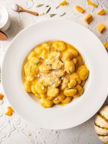 Butternut squash pasta gnocchi in a bowl topped with parmesan cheese and rosemary.
