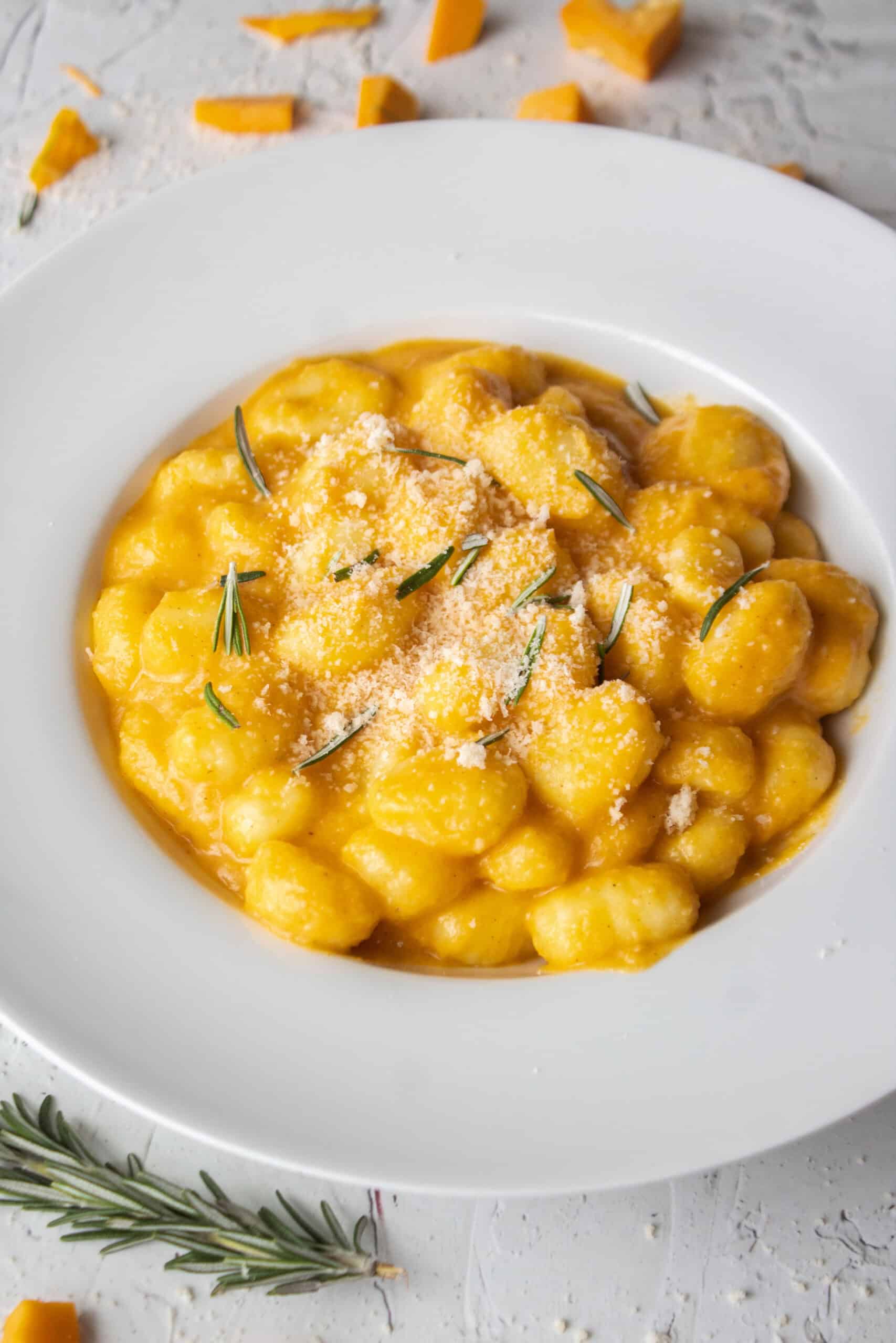Butternut squash pasta gnocchi in a bowl topped with parmesan cheese and rosemary.