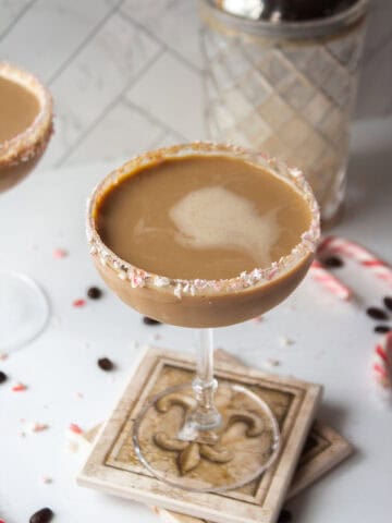 Chocolate peppermint espresso martini in a coupe glass rimmed with crushed candy canes on coasters.