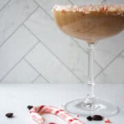 Close up of chocolate peppermint espresso martini in a coupe glass rimmed with crushed candy canes on coasters.
