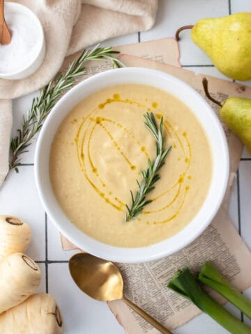 Pear and roasted parsnip soup in a white bowl garnished with rosemary and a drizzle of olive oil.